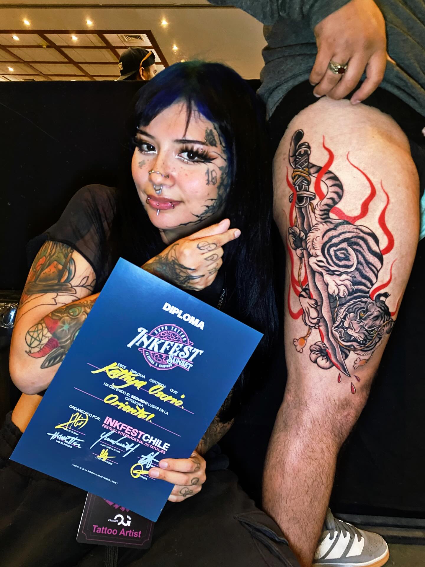 Nea Aurora mostrando un diploma junto a un tatuaje de tigre premiado