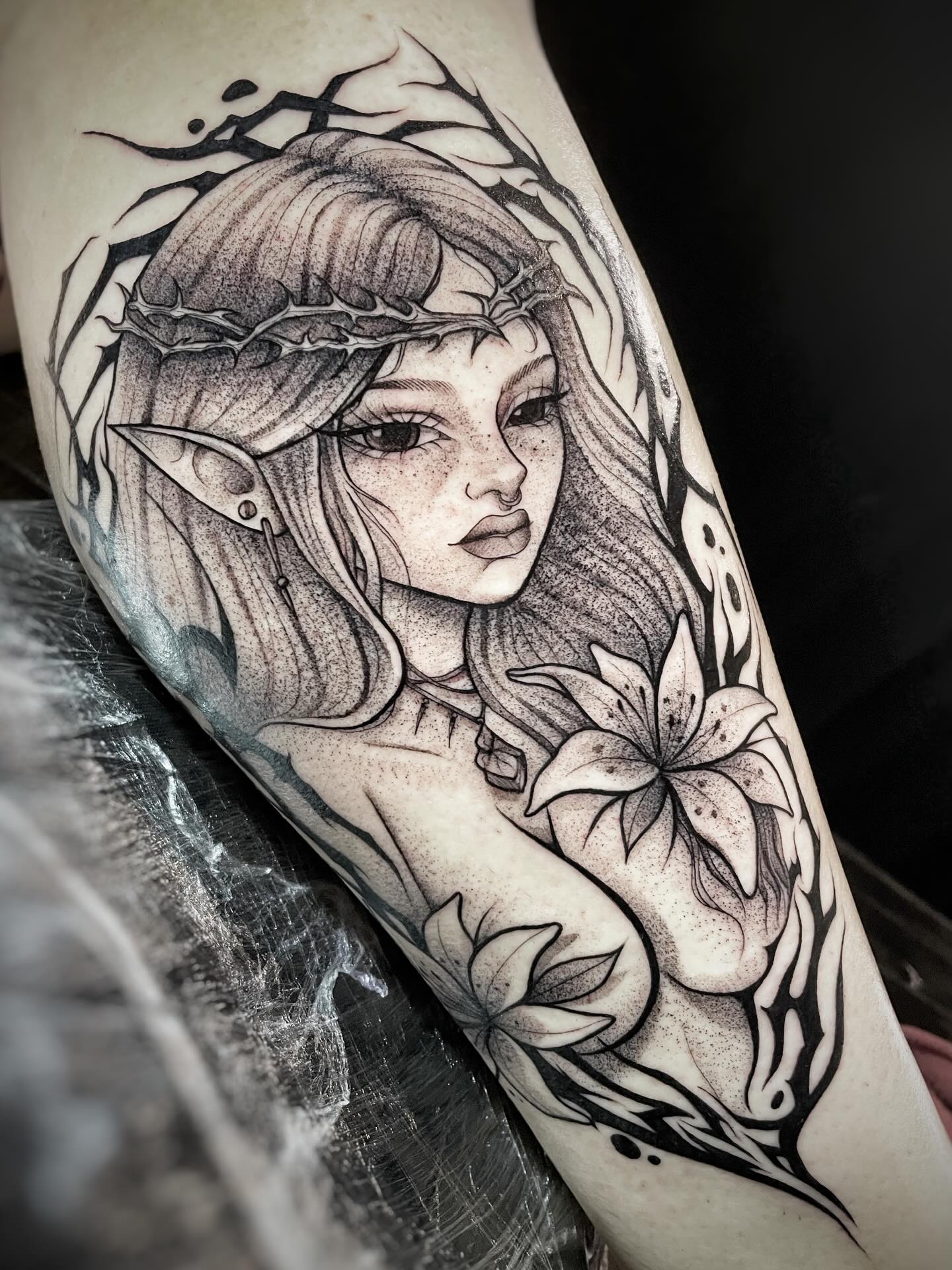 Tatuaje dark gothic de elfa con corona de espinas y lirios en el brazo