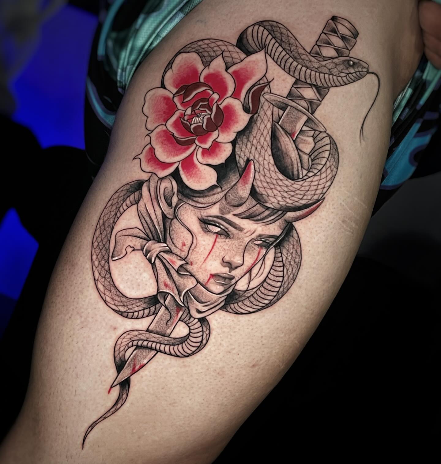 Tatuaje en negro y rojo de mujer demonio con serpientes, rosa y daga en el muslo