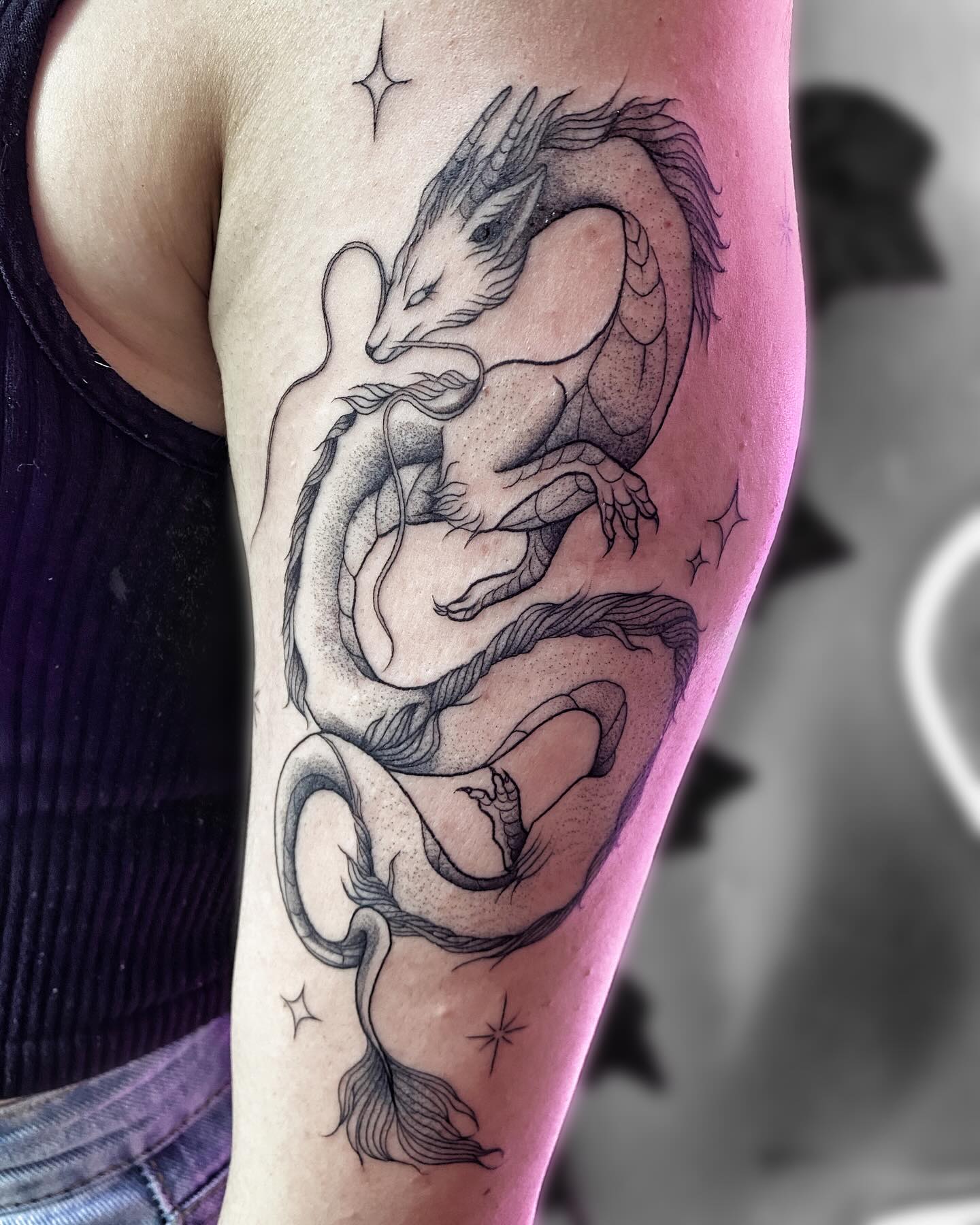 Tatuaje de dragón entrelazado con sombreado de puntillismo y pequeñas estrellas en el brazo