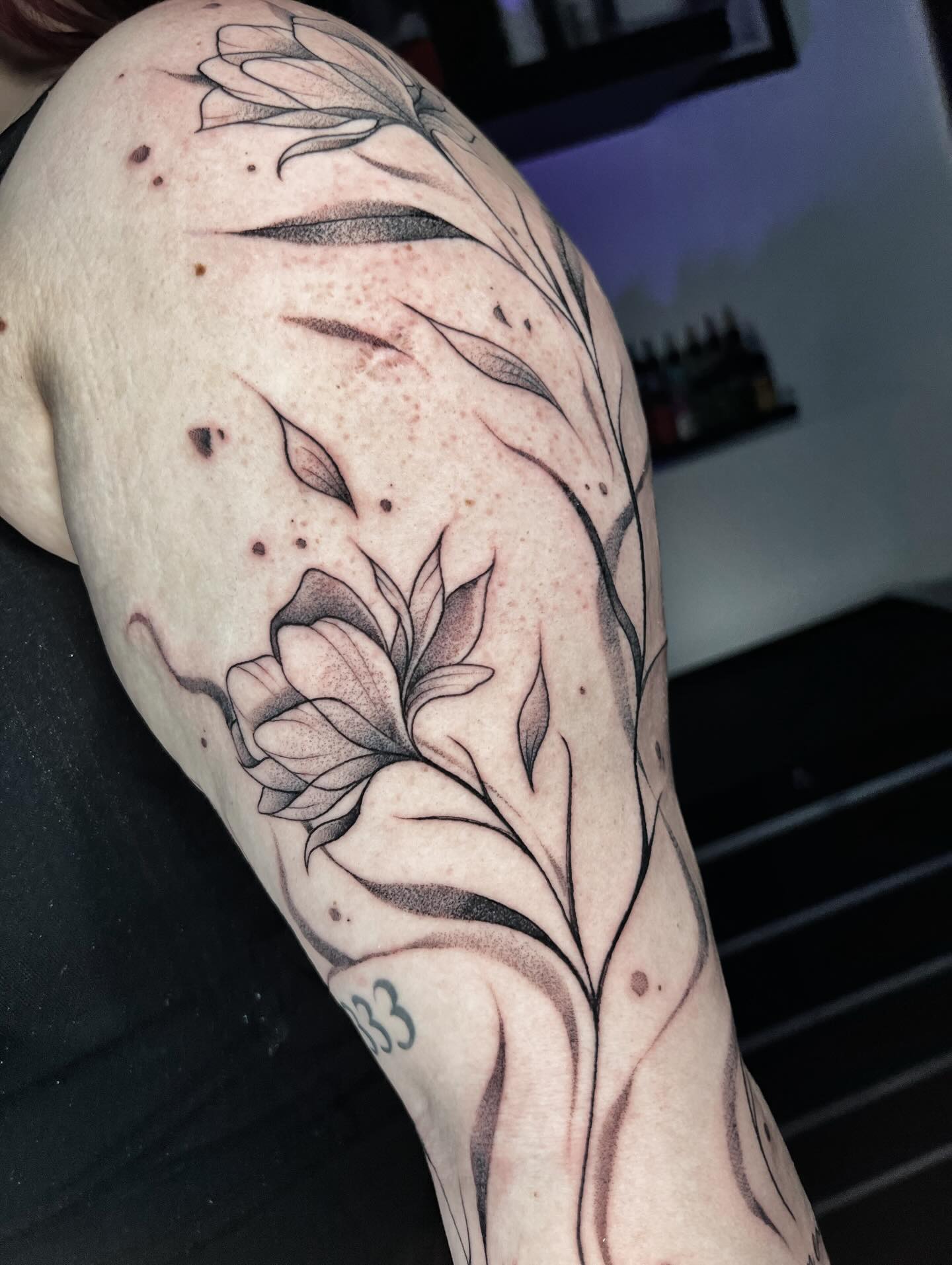 Tatuaje floral de líneas orgánicas y sombreado fino sobre hombro y brazo