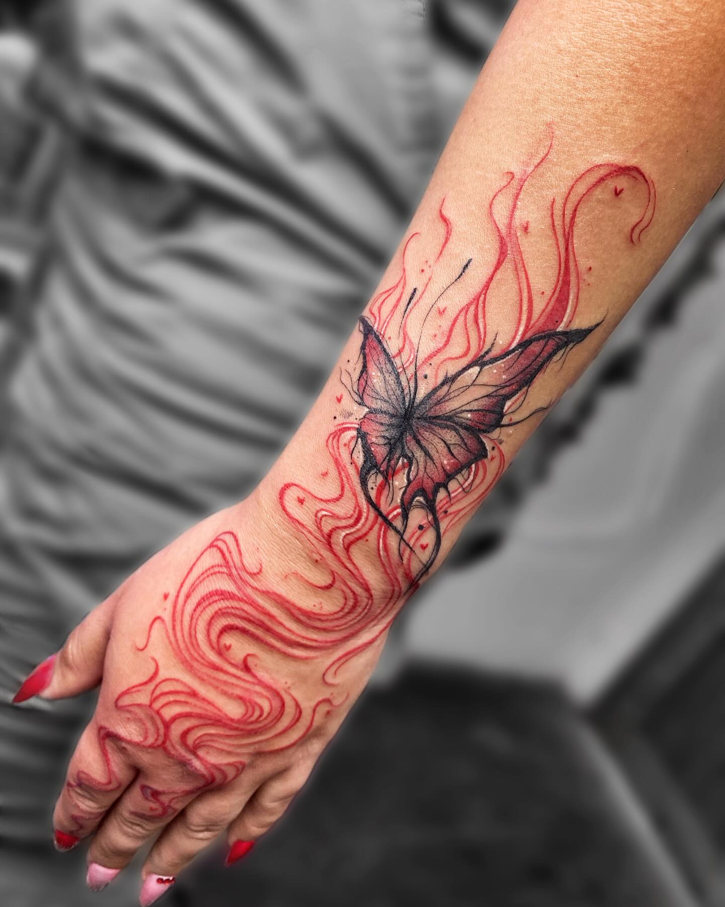 Tatuaje fine line de mariposa negra y roja con líneas ondulantes sobre antebrazo y mano
