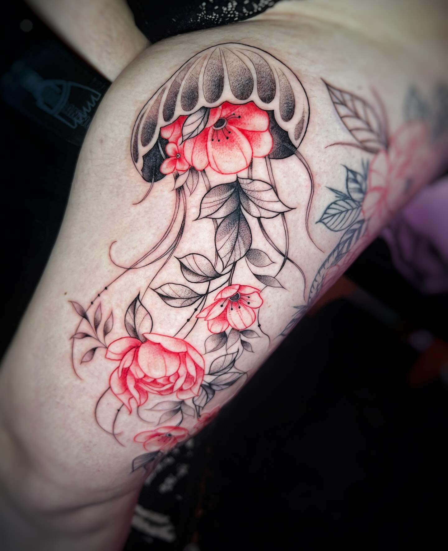 Medusa ornamental rodeada de flores rojas y hojas en fine line sobre el brazo