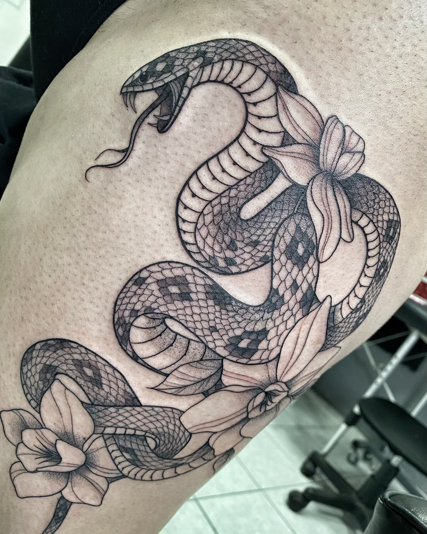 Serpiente enrollada entre flores en fine line y puntillismo sobre el muslo